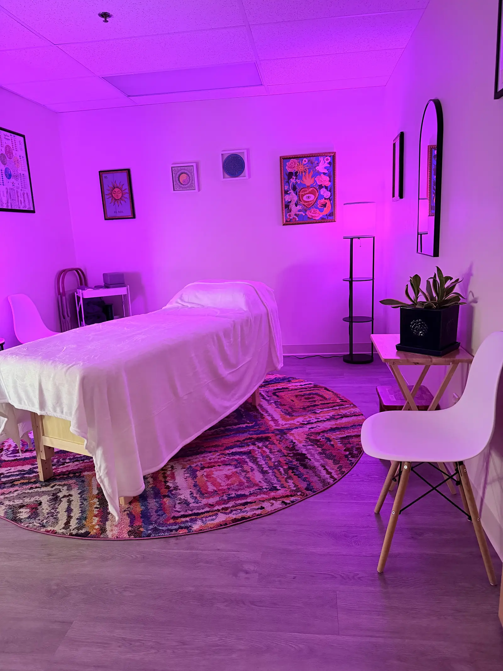 A treatment room with a draped massage table lit in bright purple ambient light.